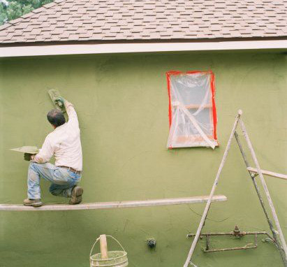 Stucco worker on side of home. Applying stucco finish.